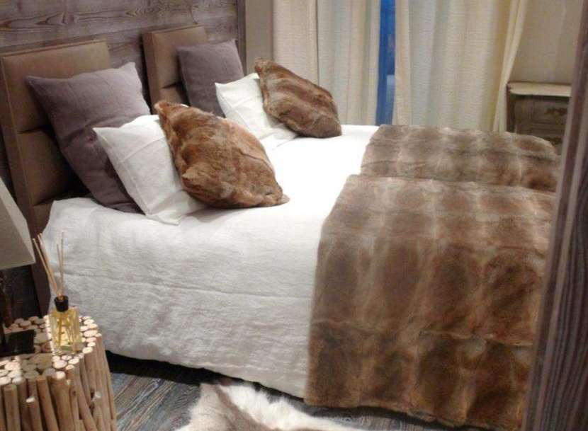 Cozy up in this rustic-chic bedroom featuring a plush fur throw and a stunning antler chandelier.