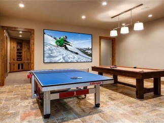 This stunning game room boasts a large projector screen perfect for movie nights, along with a ping pong table and pool table for entertainment.