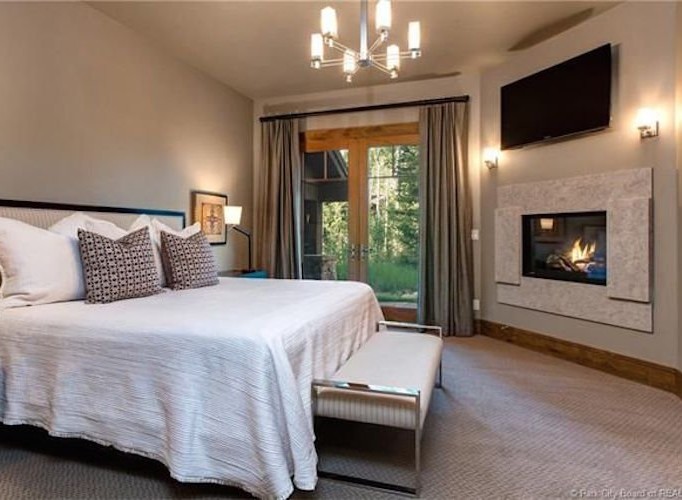 This luxurious bedroom boasts a cozy fireplace, large windows offering stunning views, and a plush bed with high-end linens.