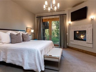 This luxurious bedroom boasts a cozy fireplace, large windows offering stunning views, and a plush bed with high-end linens.