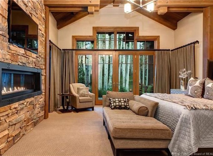 This luxurious bedroom boasts a stunning stone fireplace, large windows showcasing breathtaking views, and a comfortable chaise lounge perfect for relaxation.