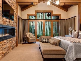 This luxurious bedroom boasts a stunning stone fireplace, large windows showcasing breathtaking views, and a comfortable chaise lounge perfect for relaxation.