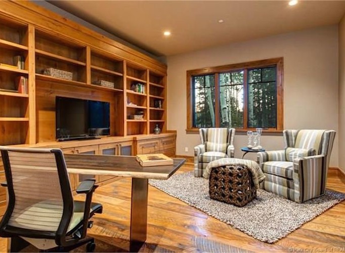 This stunning home boasts a spacious office with custom built-in shelving, hardwood floors, and a large window offering abundant natural light.
