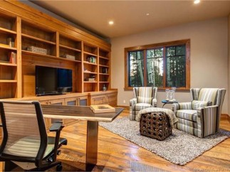 This stunning home boasts a spacious office with custom built-in shelving, hardwood floors, and a large window offering abundant natural light.
