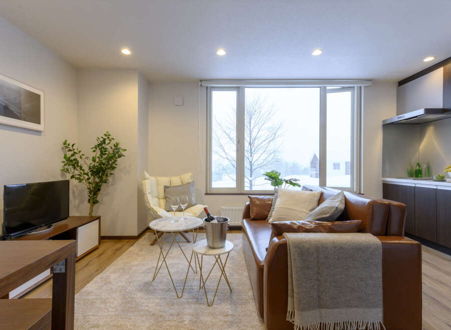 Cozy living room with a brown leather sofa, a large window overlooking a snowy landscape, and modern decor.