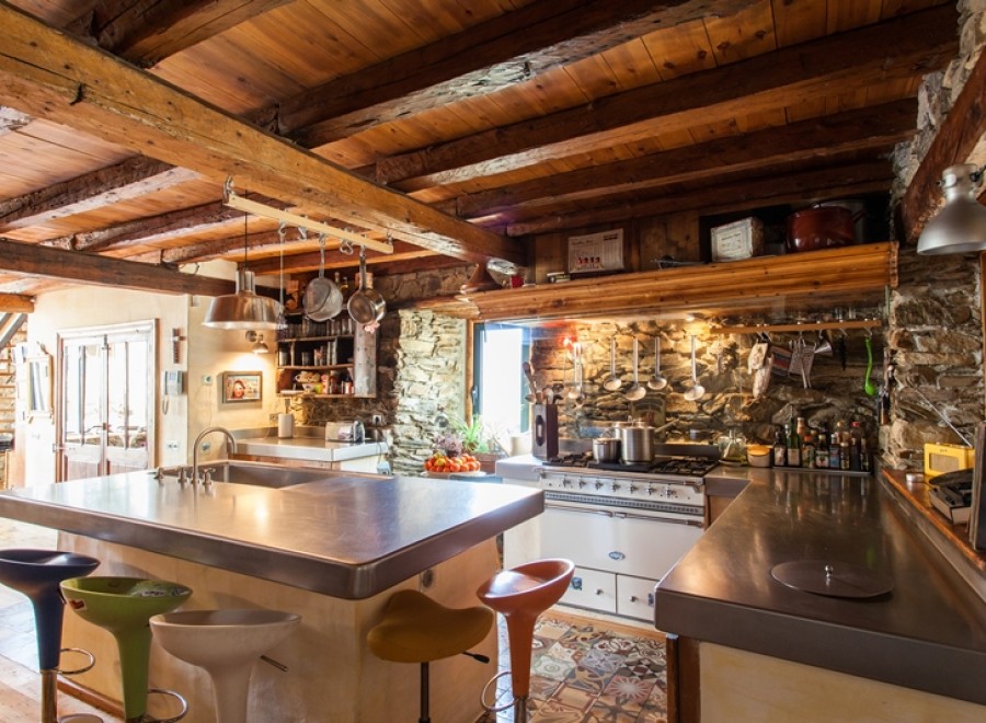 Rustic farmhouse kitchen with exposed wooden beams, stone walls, and a large stainless steel island.