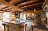 Rustic farmhouse kitchen with exposed wooden beams, stone walls, and a large stainless steel island.