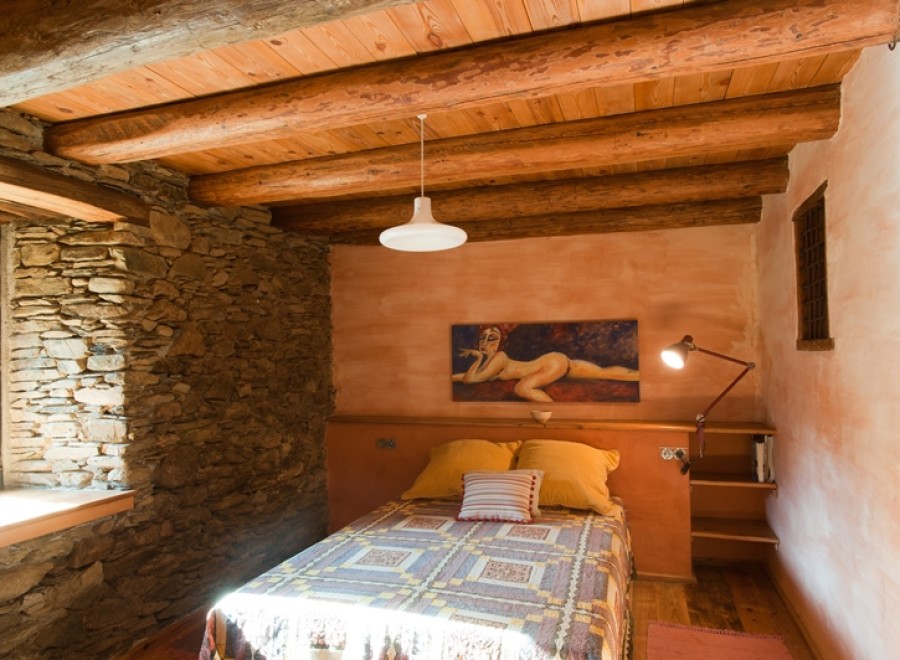 Rustic bedroom with exposed wooden beams and stone walls.