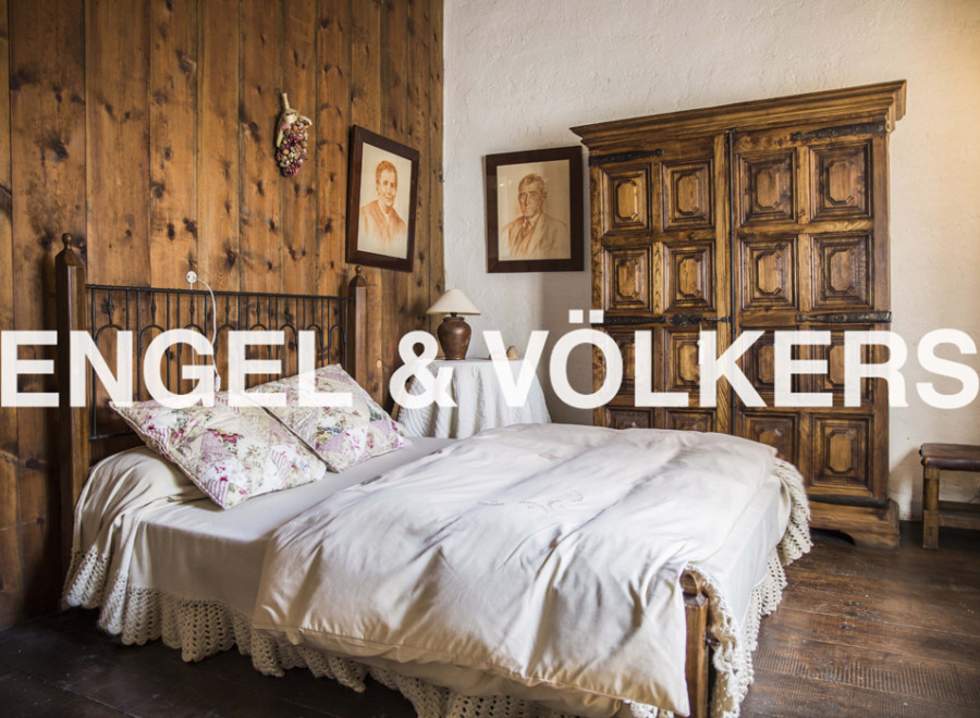 This charming bedroom boasts a rustic wooden wall, a cozy bed with crocheted details, and an antique wooden wardrobe.