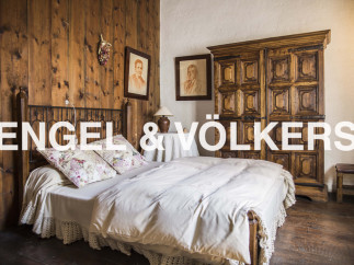 This charming bedroom boasts a rustic wooden wall, a cozy bed with crocheted details, and an antique wooden wardrobe.