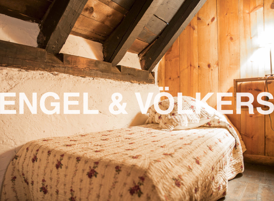 Cozy attic bedroom with exposed wooden beams and charming floral quilt.