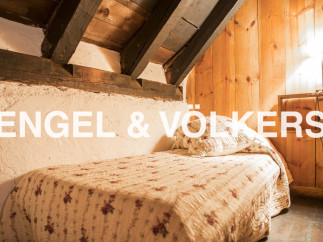 Cozy attic bedroom with exposed wooden beams and charming floral quilt.