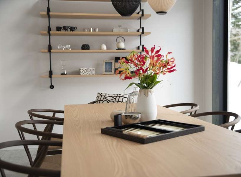 Modern dining room with light oak table, dark wood chairs, and a minimalist shelving unit displaying decorative items.
