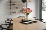 Modern dining room with light oak table, dark wood chairs, and a minimalist shelving unit displaying decorative items.