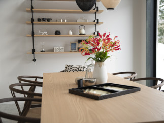Modern dining room with light oak table, dark wood chairs, and a minimalist shelving unit displaying decorative items.