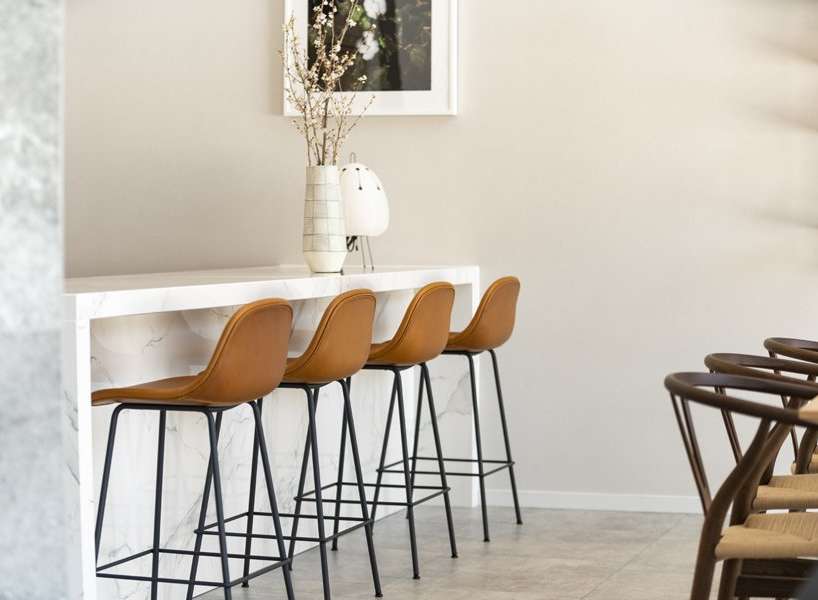 This modern kitchen boasts a sleek marble countertop breakfast bar with four stylish tan leather barstools.