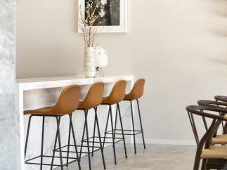 This modern kitchen boasts a sleek marble countertop breakfast bar with four stylish tan leather barstools.