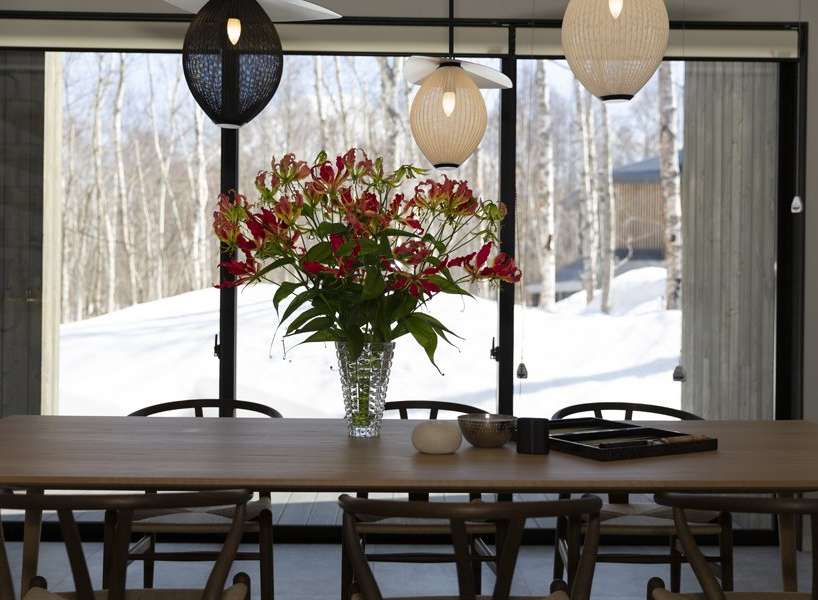 Modern dining room with large windows showcasing snowy landscape.