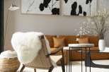 A cozy living room features a stylish woven chair with a sheepskin throw, complemented by a warm orange velvet sofa and minimalist side tables.
