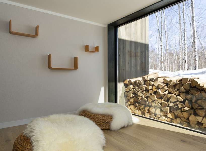 Cozy living space featuring floor seating with fluffy sheepskin throws and woven baskets, complemented by minimalist wooden shelves on a neutral wall.