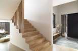 Modern minimalist home showcasing a stunning light oak staircase with sleek wooden railing, leading to an open-plan living area.