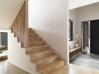 Modern minimalist home showcasing a stunning light oak staircase with sleek wooden railing, leading to an open-plan living area.