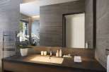 This luxurious bathroom boasts a sleek, modern design with dark gray tile, a large mirror, and a spacious vanity with a dark countertop.