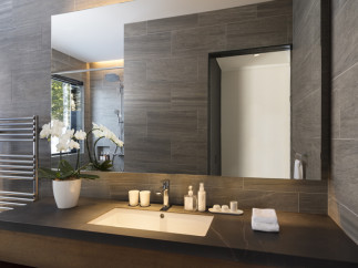 This luxurious bathroom boasts a sleek, modern design with dark gray tile, a large mirror, and a spacious vanity with a dark countertop.