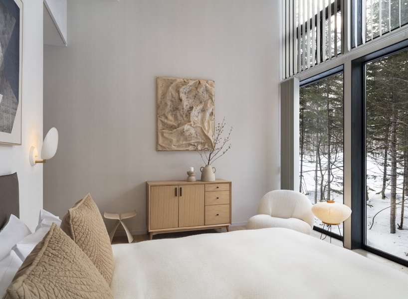 This bedroom boasts a minimalist design with a light and airy feel, featuring large windows showcasing a snowy forest landscape.