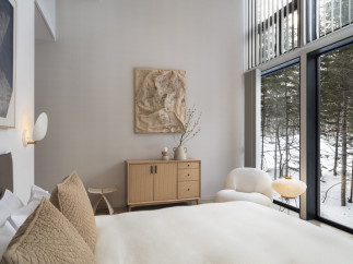 This bedroom boasts a minimalist design with a light and airy feel, featuring large windows showcasing a snowy forest landscape.