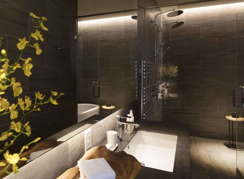Luxurious bathroom with dark tile, a spacious shower with multiple shower heads, and a modern soaking tub.