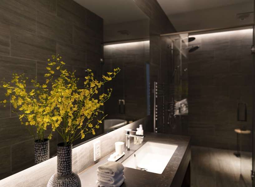 Luxurious bathroom with dark gray tile, modern sink and fixtures, and yellow orchids adding a touch of elegance.
