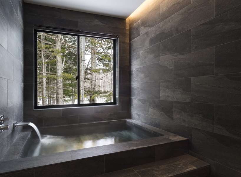 Indulge in tranquility with this stunning bathroom featuring a built-in soaking tub and a large window showcasing breathtaking views of a snow-covered forest.