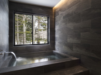 Indulge in tranquility with this stunning bathroom featuring a built-in soaking tub and a large window showcasing breathtaking views of a snow-covered forest.
