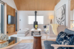 This stunning living room boasts a vaulted wood ceiling, large windows offering abundant natural light, and a cozy fireplace as a focal point.