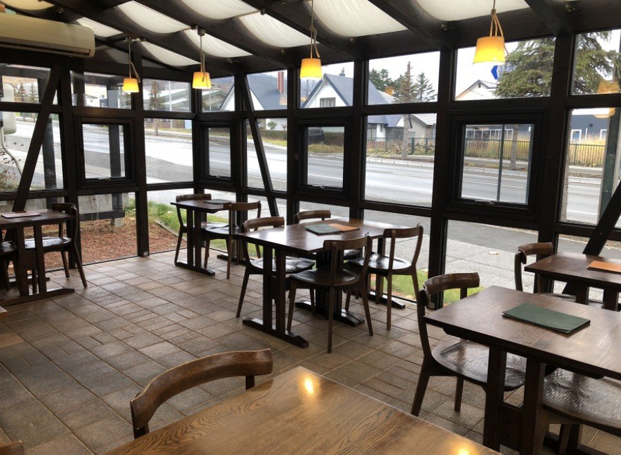 This sunroom restaurant boasts a rustic-chic design with dark wood tables and chairs, complemented by soft, warm lighting.