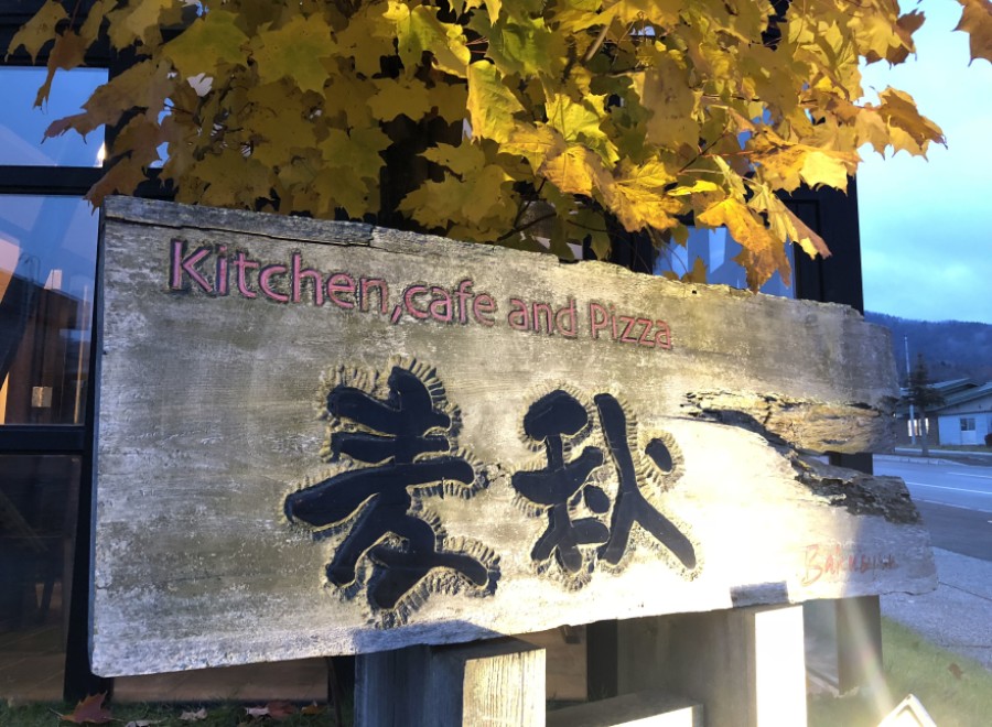 A rustic wooden sign for a Kitchen, Cafe and Pizza restaurant is illuminated at night.