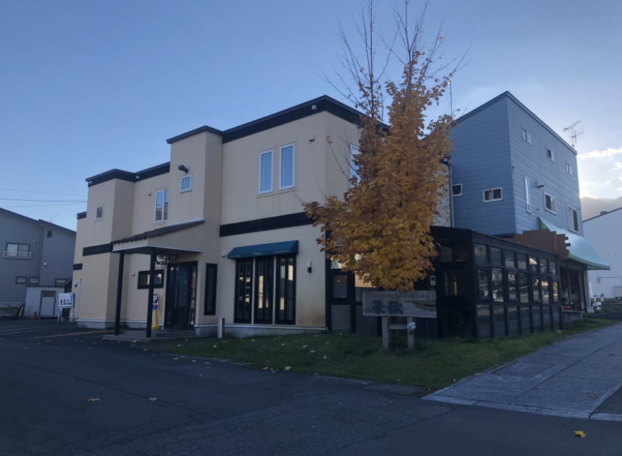 This charming two-story building features a light beige exterior with dark brown accents, complemented by a vibrant yellow tree in the foreground.