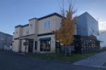 This charming two-story building features a light beige exterior with dark brown accents, complemented by a vibrant yellow tree in the foreground.