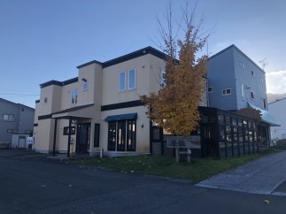 This charming two-story building features a light beige exterior with dark brown accents, complemented by a vibrant yellow tree in the foreground.