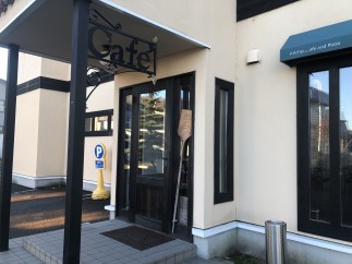 This charming cafe boasts a quaint exterior with a welcoming entrance, marked by a stylish "Cafe" sign and a convenient parking spot nearby.