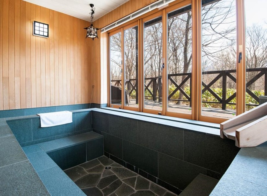 Relax in this serene private onsen bath, featuring a spacious soaking area with stone tiling and a wooden water channel.