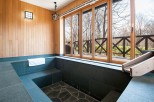 Relax in this serene private onsen bath, featuring a spacious soaking area with stone tiling and a wooden water channel.