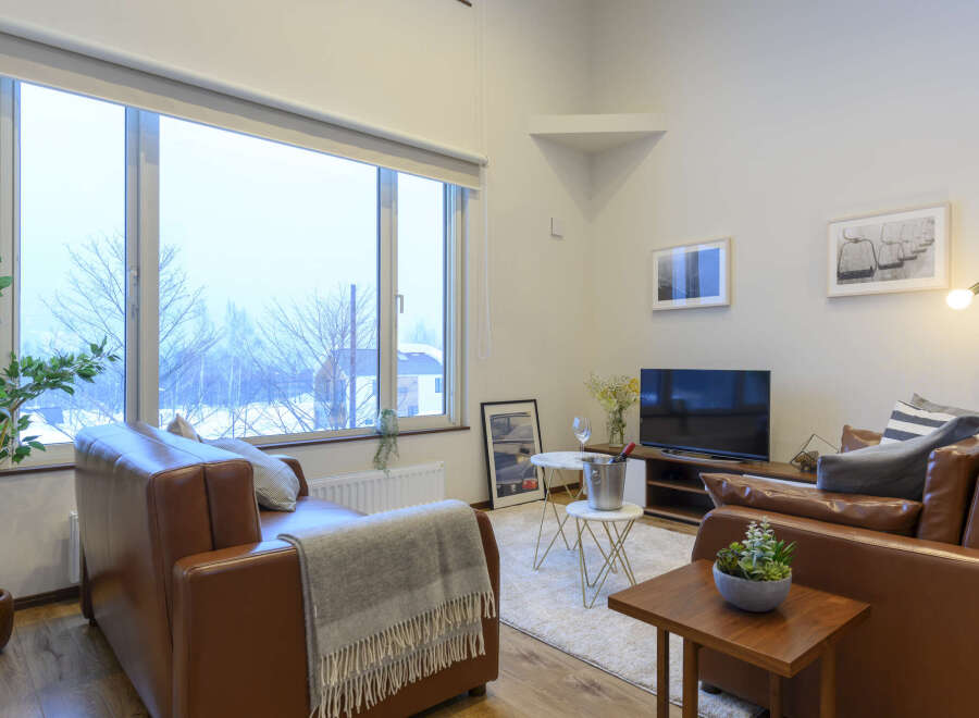 Cozy living room with large windows offering scenic views, leather sofas, and modern decor.
