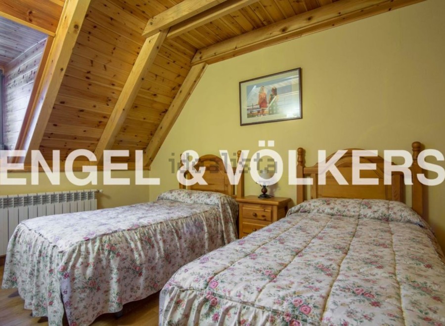 Charming attic bedroom with twin beds, featuring a wooden beamed ceiling and floral bedding.