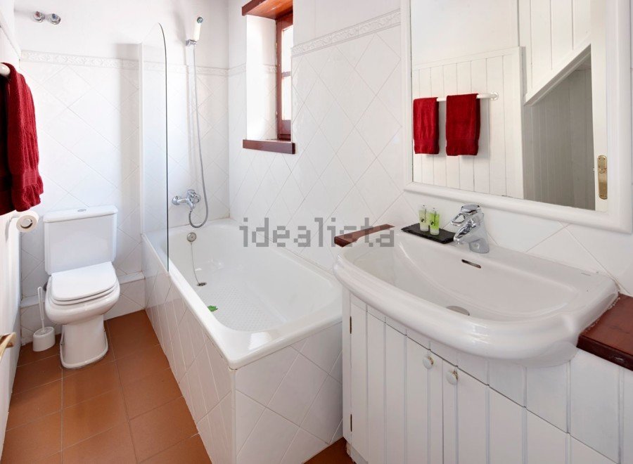 This charming bathroom boasts a classic white tile design, complete with a bathtub and a separate toilet.