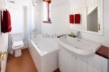 This charming bathroom boasts a classic white tile design, complete with a bathtub and a separate toilet.