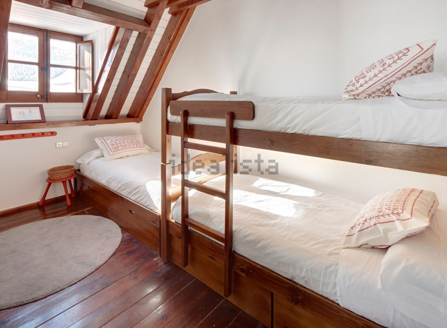Cozy attic bedroom with wooden bunk beds and a single bed, perfect for a family getaway.