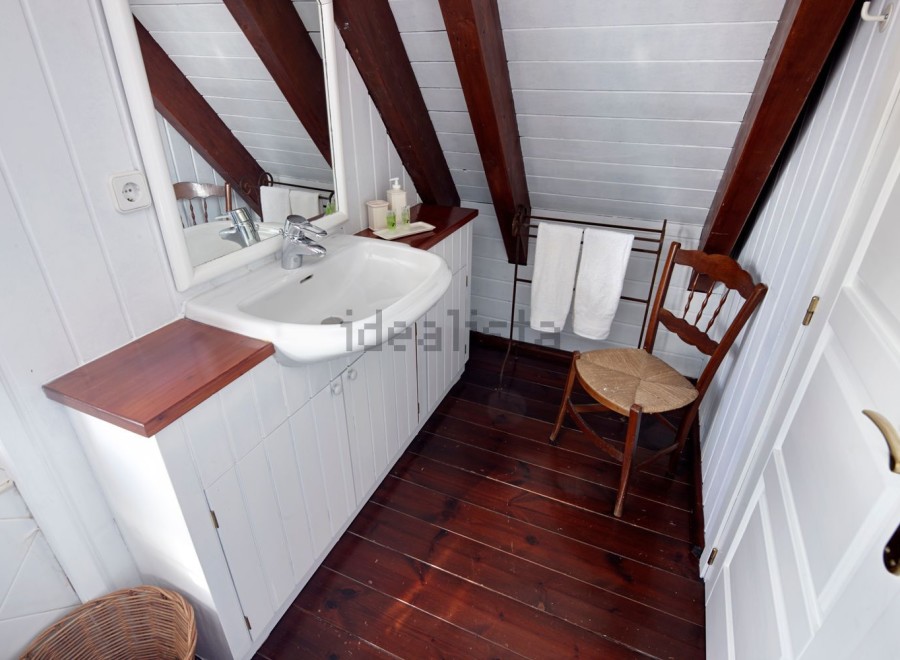 Charming attic bathroom with white cabinets and wooden floors.