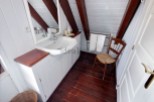 Charming attic bathroom with white cabinets and wooden floors.